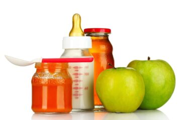 Przykładowe pokarmy dla niemowlaka: butelka ze smoczkiem z mlekiem, dwa zielone jabłka i słoiczek z papką dla niemowląt.