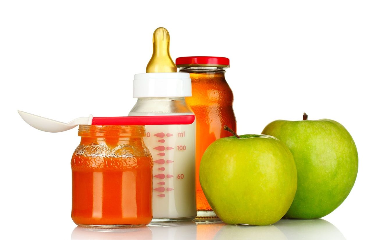 Przykładowe pokarmy dla niemowlaka: butelka ze smoczkiem z mlekiem, dwa zielone jabłka i słoiczek z papką dla niemowląt.